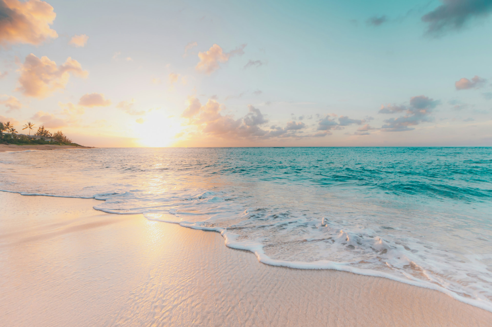 Serene tropical shoreline at sunrise with turquoise waves washing onto pale sand